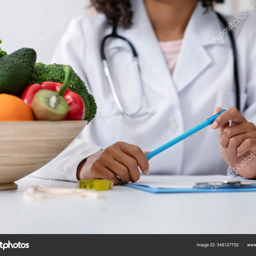 Cropped of african female doctor dietologist holding pen, taking notes, working at clinic